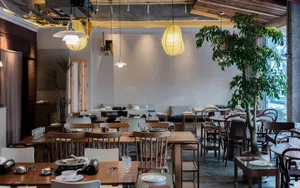Industrial restaurant interior with wooden tables, concrete walls, glass windows, and hanging paper lanterns.