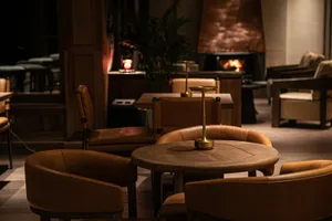 A cozy restaurant interior with leather chairs, walnut tables, and a warm copper fireplace.