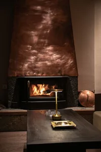 A cozy living room with a metallic copper fireplace, featuring wood and stone accents and a table with a brass candle holder.
