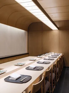 A minimalist restaurant interior with long wooden tables, chairs, and a sleek design.
