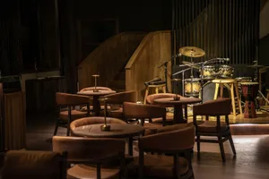 A modern restaurant interior featuring wooden tables, leather chairs, and metal drum set.
