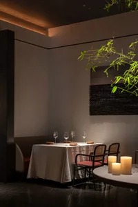 A minimalist restaurant interior featuring wooden tables, leather chairs, and a stone floor.