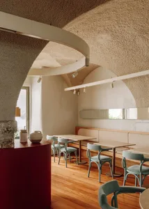 A modern cafe interior with concrete walls, wooden flooring, and teal dining chairs