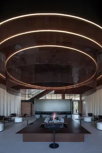 An industrial-style lobby with brick walls, metal railings, and a glass ceiling, featuring a central fire pit.