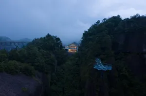 A modern house built on a cliff with a glass extension overlooking a mountainous landscape.