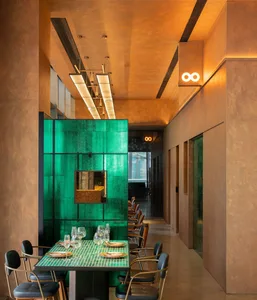 A modern restaurant interior features a green glass wall with a metallic accent and sleek, black chairs with metal frames.