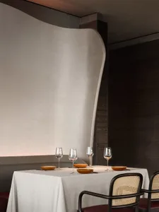 A minimalist restaurant interior showcasing concrete walls, sleek tableware, and elegant seating arrangements.