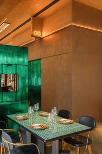 Modern minimalist restaurant interior with green tiled tables and brown walls.