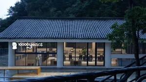 A minimalist restaurant with concrete walls and large windows, featuring modern furniture and a clean design.