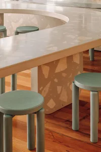 A modern cafe interior with a terrazzo countertop and wooden stools.