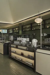 Coffee shop production counter with metal countertop, glass shelves, and hanging lantern light fixtures.