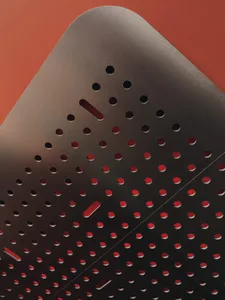 A modern metal object with holes and red lines on a red background.