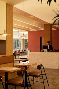 A modern cafe interior with wooden tables and chairs, red walls, and a counter area.