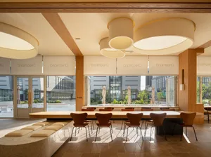 A modern cafe interior with wooden tables and chairs, round pendant lights, and large windows.