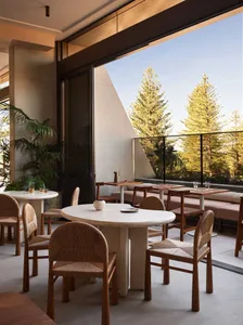Circular dining tables with woven chairs on a patio made of concrete, surrounded by lush greenery and trees.