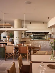Modern restaurant interior featuring wood tables, stone flooring, glass walls, and leather chairs.