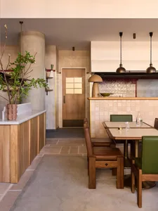 Interior of a rustic coffee shop featuring wooden furniture, a concrete counter, and ceramic tiles on the walls.