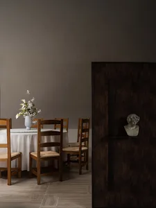 Modern dining room with wooden chairs and a table, featuring a vase of flowers and a bust on a shelf.