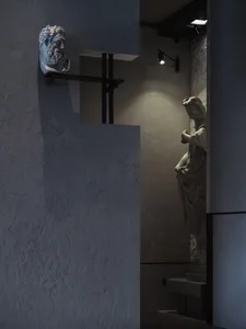 A sculpture displayed in a concrete interior space, illuminated by a spotlight.