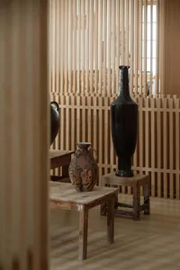 Decorative ceramic vases placed on wooden stools and tables in a room with wooden slat walls.