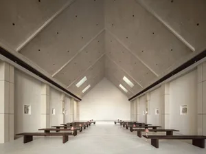 A minimalist, modern church interior with concrete walls and floors, high ceiling, and natural light.