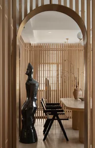 A modern dining room featuring timber slat dividers, black chairs, and a black statue.