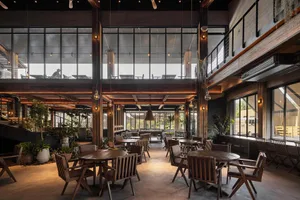 Modern industrial-style cafe with wooden tables, concrete flooring, and glass walls.