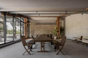 A modern meeting room featuring concrete walls and wooden furniture, with large windows allowing natural light.