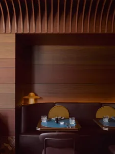 A modern restaurant booth made of wood with a sleek design, featuring plush seating and a small table with glasses and cutler