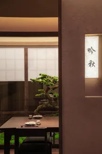 A minimalist restaurant interior with a wooden dining table, concrete floor, and paper lantern hanging on the wall.