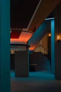 A modern, minimalist interior design featuring exposed concrete walls and floors, with a spiral staircase and ambient lightin