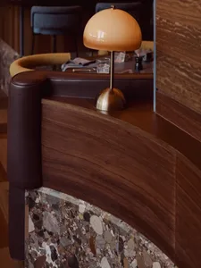 A modern restaurant bar counter with marble floor, wooden finishes, and a brass pendant lamp.