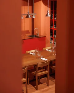 A wooden dining table set for four people in a restaurant interior, with pendant lights and wine racks in the background.