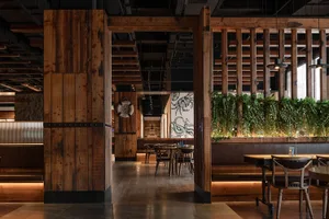 Industrial-themed restaurant interior with wooden elements and hanging green plants.