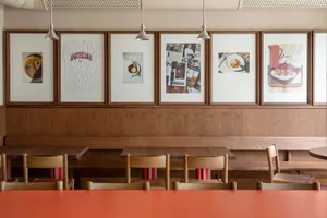 A modern restaurant interior featuring wooden tables, chairs, and benches with framed artworks on the wall.