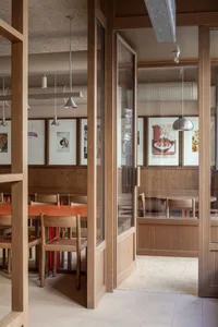 A modern restaurant interior with wooden tables and chairs, framed artwork, and industrial-style lighting.