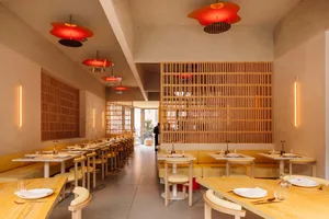 A modern restaurant interior with wooden tables, chairs, and booths. The space features contemporary design elements and an i
