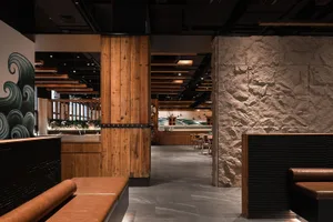 A stylish modern restaurant interior featuring wooden furniture, stone walls, and leather seating.
