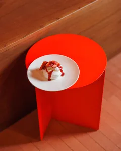 A metallic red table with a white plate containing a dessert with strawberries and a drizzle of sauce.