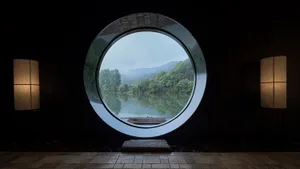 A minimalist window overlooking a serene lake surrounded by trees and mountains, with two fabric lampshades on either side.