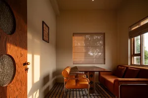 A cozy indoor living room featuring orange upholstered furniture, a wooden table, and a large window with natural light.