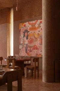 A café interior with a warm color palette, featuring chairs and tables arranged around a round table, and a colorful mural on