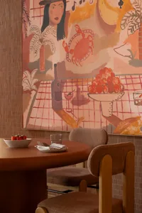 A modern restaurant interior with a table set for a meal, featuring a painting of a woman on the wall and various food items