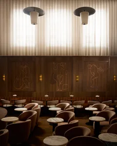 A modern bar and restaurant interior with wood-paneled walls, marble tables, and fabric-covered chairs.