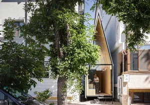A modern residential exterior featuring wooden and glass elements and surrounded by green foliage.