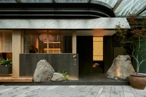 A modern restaurant exterior featuring large stones and a stone wall with a sign.
