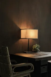 A modern desk lamp with a wooden base and a fabric lampshade illuminated in a home office setting.