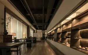 Long shot of a modern restaurant interior with wooden tables, chairs, and concrete walls.