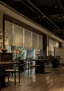 Interior of an industrial-themed restaurant with wooden tables and chairs, glass walls, and natural light.