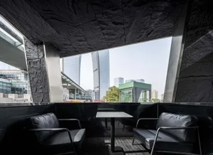 Modern industrial restaurant terrace made of concrete with metal seating and a large window overlooking urban buildings.